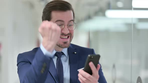 Excited Young Businessman Celebrating Success on Smartphone alt