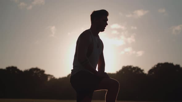 Man Stretching His Legs Before a Run Whilst Being Silhouetted By The Evening Sun alt