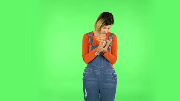 Girl Stands and Thinks, Then Intently Writes with Pencil in Notebook. Green Screen alt