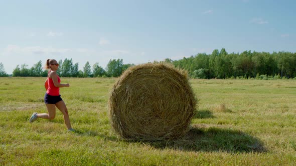 An Elegant Girl in the Summer in the Field Jumps on a Haystack