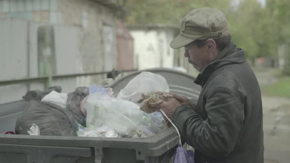 A Beggar Homeless Man Tramp Is Looking for Food in a Trash Can. Kyiv. Ukraine alt