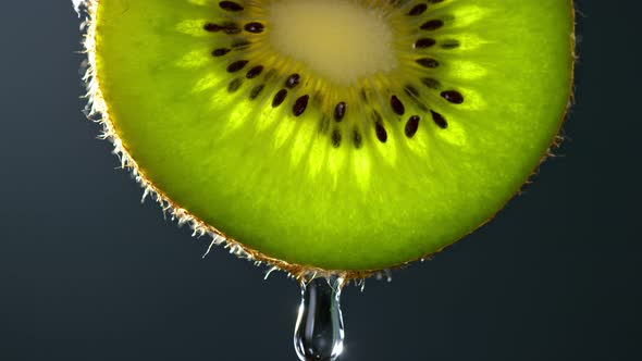Super Slow Motion Macro Shot of Water Drop Falling From Kiwi Slice on Grey Background at 1000Fps alt