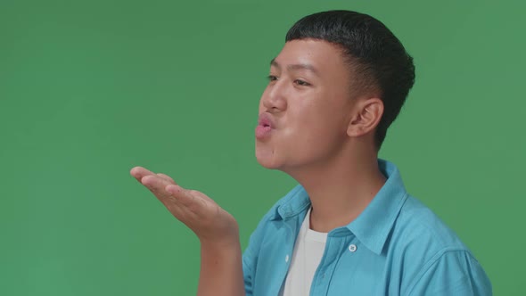 Side View Of Young Asian Boy Blowing Kisses To A Camera In The Green Screen Studio alt