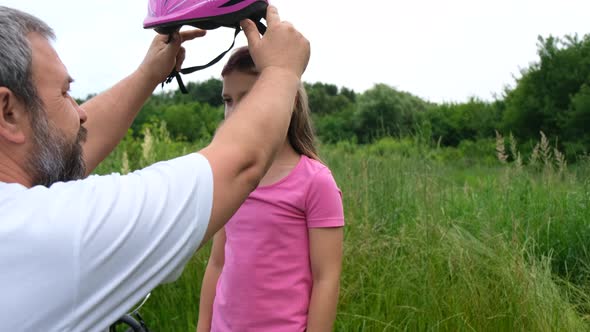 A loving father puts a Bicycle helmet on his daughter. Safe Cycling.