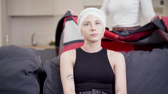 Sad Young Woman Sitting on Couch Thinking As Unrecognizable Friend Passing Covering Ill Lady with alt