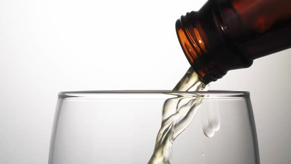 Beer is pouring with bubbles and foam in large beer glass from bottle on white background close up. alt