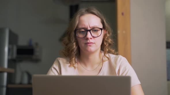 Woman with Glasses is Sitting at Laptop and Texting with Someone or Preparing Work Report alt