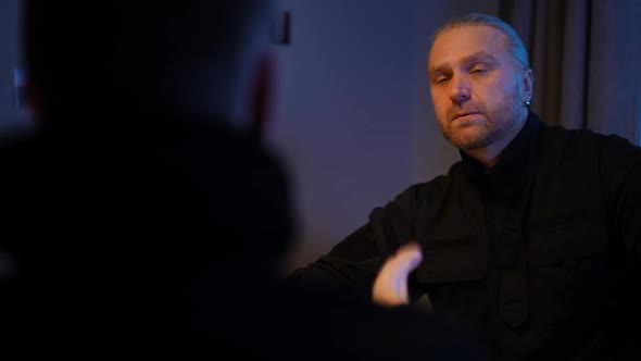 Portrait of Caucasian Policeman Smoking Listening to Witness Gesturing Talking Sitting at Table alt
