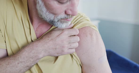Happy caucasian mature man showing plaster on arm where he was vaccinated against coronavirus alt