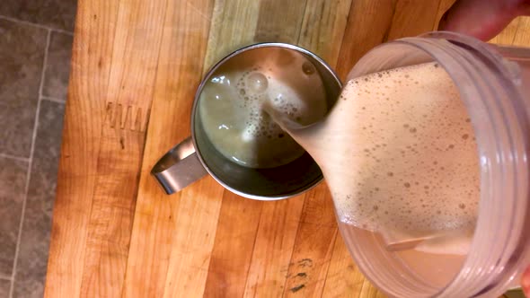 Bulletproof ketogenic coffee with butter is being poured from a blender to a stainless steel cup alt