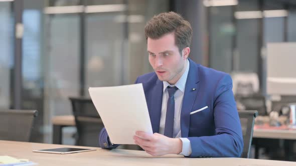 Businessman Upset While Reading Documents in Office alt