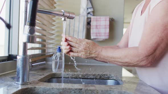 Mid section of senior caucasian woman washing her hands in the sink at home alt