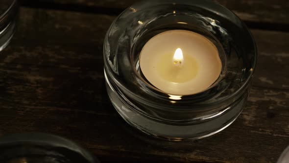 Tea candles with flaming wicks on a wooden background - CANDLES 003 alt