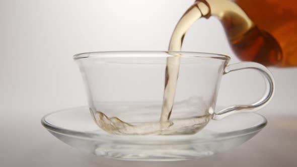 Tea Flows In A Tea Cup From A Transparent Teapot