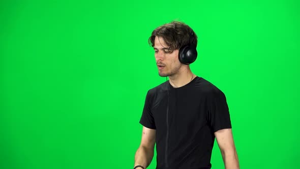 Man in Big Headphones Goes and Dances with Smartphone on Green Screen at Studio. Slow Motion alt