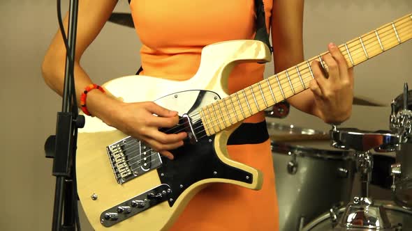 Beautiful girl plays the electric guitar. Musician in a bright orange dress