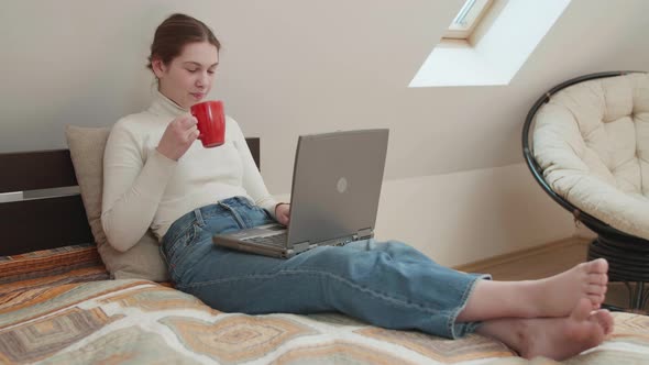 Young girl works remotely from home on bed at the computer. alt