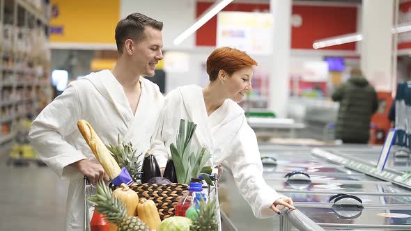Young Redhead Female Choosing Frozen Products in Supermarket Walk in Market Wearing Bathrobes