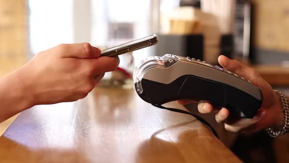 Macro unknown hand giving terminal to visitor for mobile phone payment indoor. Client hand paying 