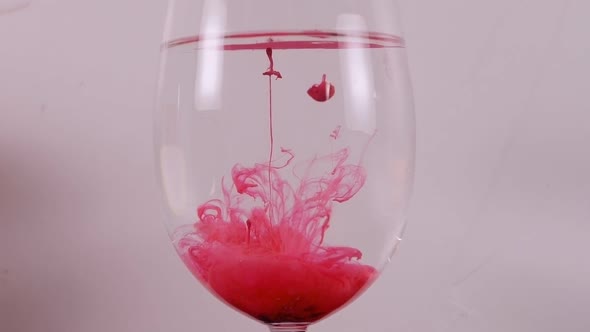 Red Ink Swirls in a Wine Glass Against a White Background alt