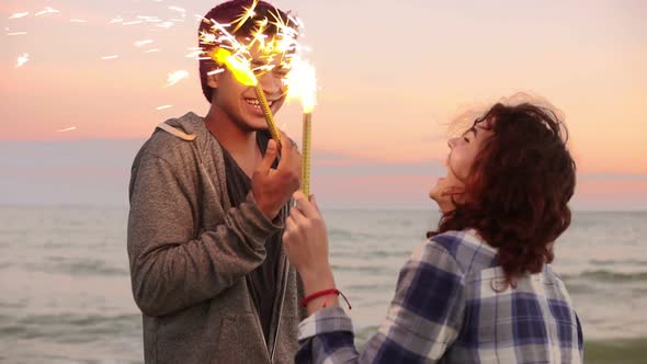 Cheerful Smiling Multiethnic Couple Holding Burning Sparkling Candles Standing By the Sea During alt