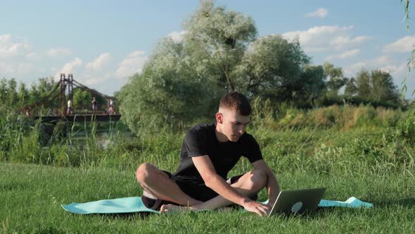 Focused man practicing yoga outdoors. Man training yoga pose in park, watching online yoga guiding alt