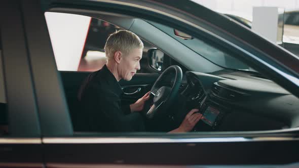 Stylish Girl Sitting in the Car Evaluates the Interior of the Car Inside alt