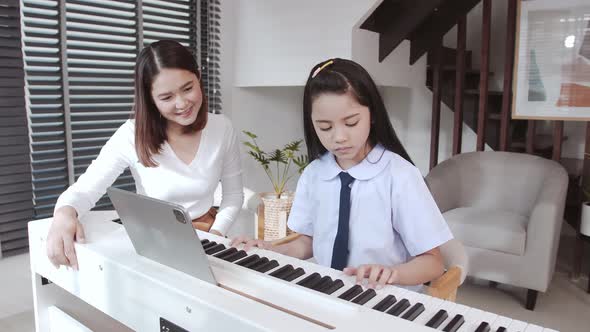 Mother accompanying daughter during virtual piano lessons. alt