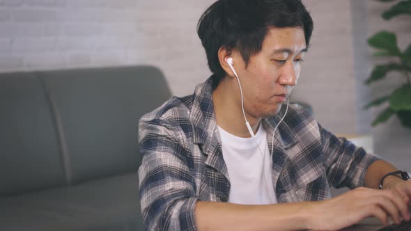 Young Asian Male Entrepreneur in Casual and Earphone Work on Computer Laptop at Late Night From Home alt