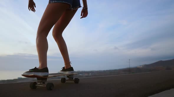 Girl on a Skateboard Ride on the Road Against the Rock and Sky During Sunset alt