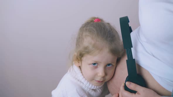 Cute Girl Listens To Baby in Mother Tummy with Headphones alt