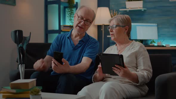 Grandparents Using Smartphone and Digital Tablet at Home alt