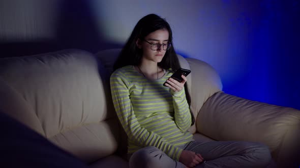 Late at night, a young brunette is sitting at the TV with a phone in her hands, camera movement alt