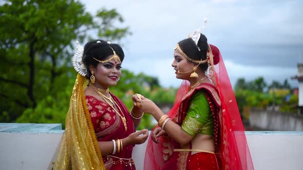 Two cheerful Indian bengali brides laughing together and talking outdoor cloudy sky alt