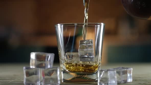 old single malt whiskey is poured from bottle into a clear glass with ice cubes. alt