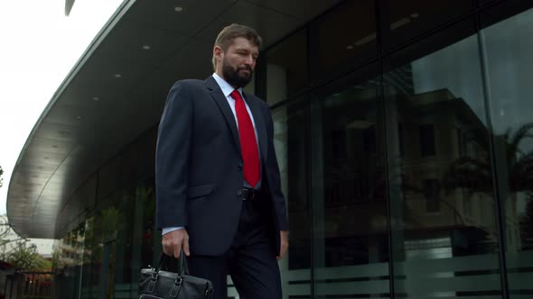 Senior Businessman in an Expensive Suit with a Briefcase in His Hand Walks Along the City Street at alt