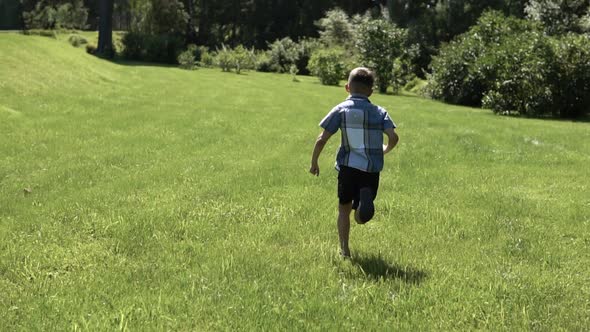 An Attractive Boy Runs Along the Grass in the Park Having a Good Mood in the Summer alt