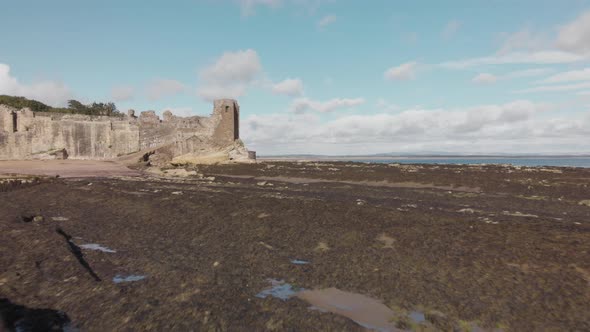 Aerial drone view approaching St Andrews Castle, flying very low to the rocky ground surrounding St alt