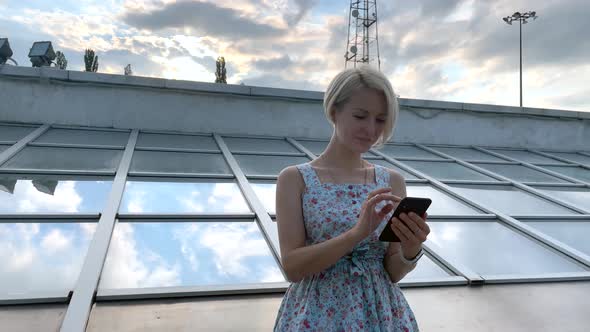 Beautiful Blonde Uses a Smartphone in the City and Smiles