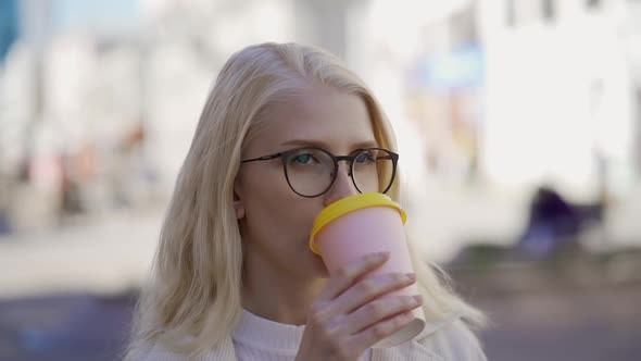 Young Stylish Woman in Glasses Drinks Delicious Coffee on the Street alt