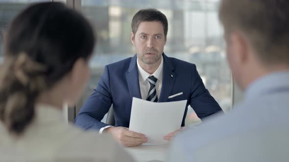 Rear Back View of Couple Having Explanation From Middle Aged Businessman alt