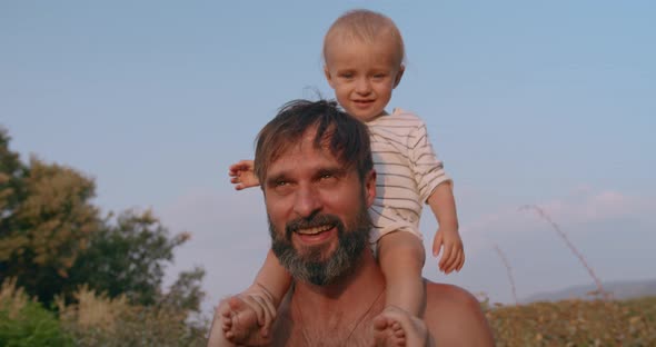 Happy Little Boy Sits on Young Father Neck and Have Fun Together Outdoor