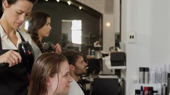 Two hairdresser blow drying their client hair alt