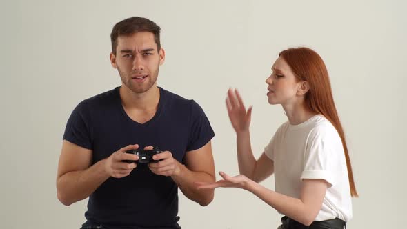Studio Portrait of Angry Frustrated Girlfriend Screaming at Addicted Boyfriend Holding Game Joystick alt