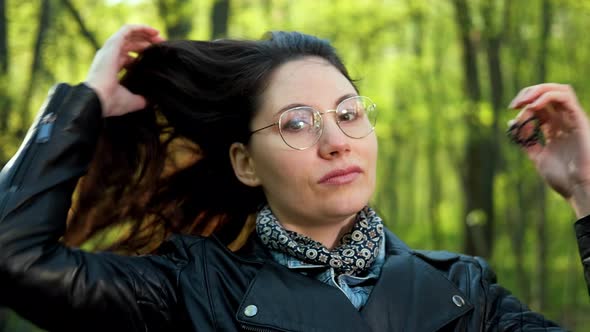 Woman with Glasses is Letting Down Her Lush Hair in the Park alt