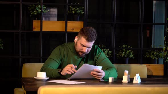 Bearded Hipster Signs Papers Sitting in a Cafe