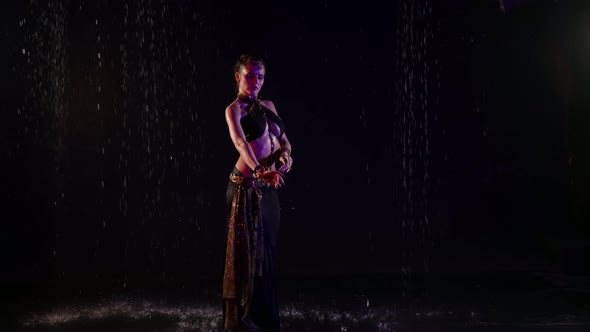 A Woman Dances an Oriental Dance on a Black Background in the Pouring Rain in the Studio alt