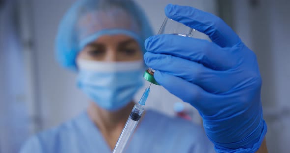 Caucasian female doctor wearing face mask preparing covid vaccine for patient alt