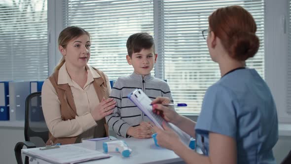 Hospital Office Female Medical Doctor Writes to the Clipboard and Measures the Temperature of alt