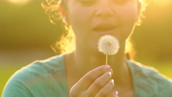 Beautiful Girl Blowing on a Dandelion Fluff Slowly Flies Through the Air alt